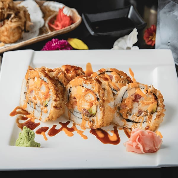 Six pieces of Zake Sushi & Ramen's fried sushi rolls with sauce, wasabi, and ginger on a white plate.
