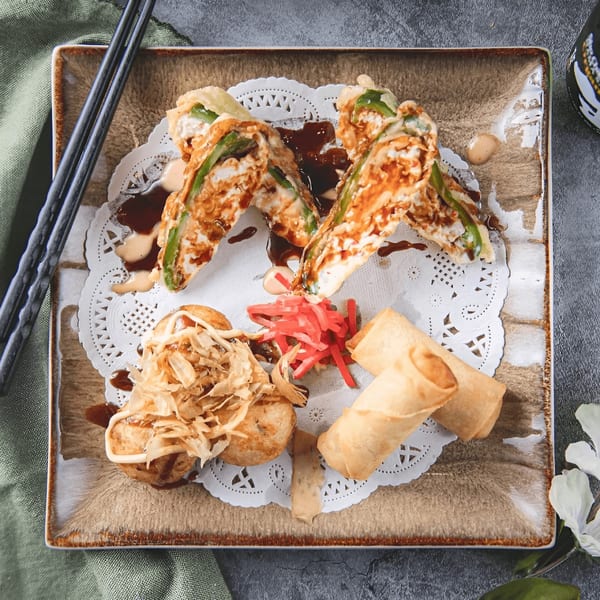 A square plate of Zake Sushi & Ramen appetizers, including tempura, takoyaki, and spring rolls.